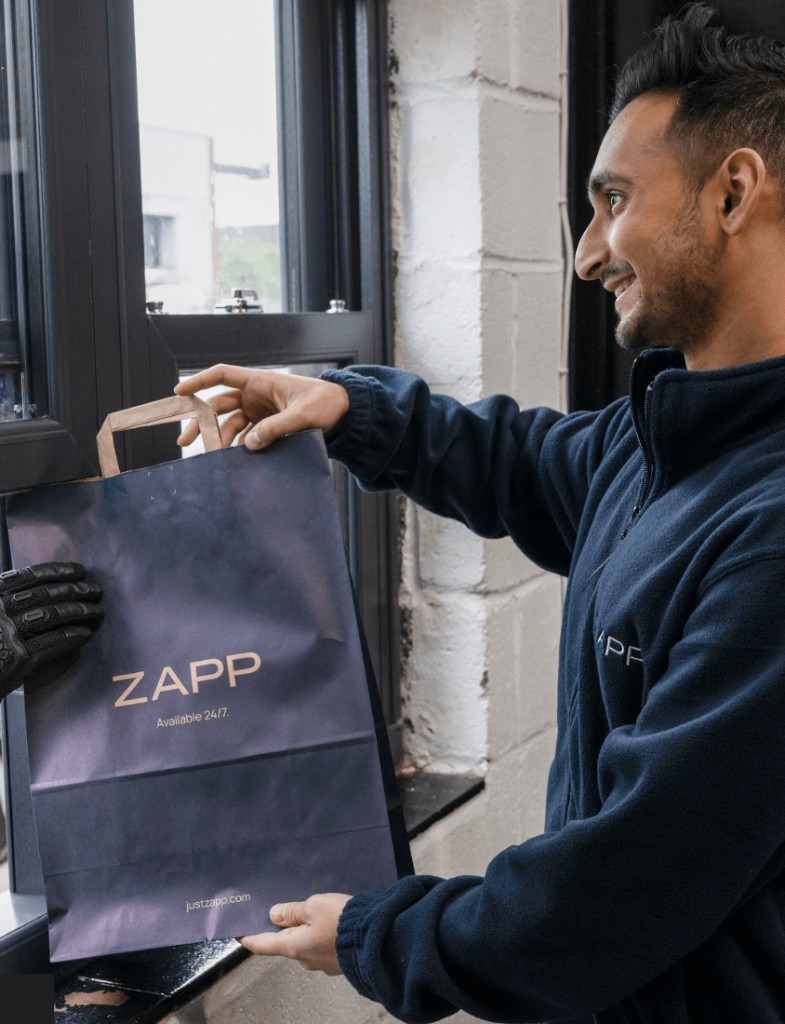 A Zapp Fulfilment Centre Associate handing a packed delivery to a rider